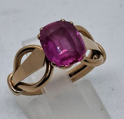 une image représentant une bague ornée d'une pierre rose posée sur une surface transparente