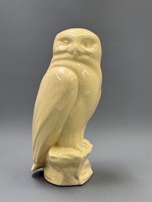 une figurine de chouette perchée sur un rocher, posée sur une surface grise