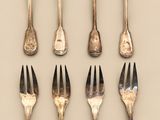 six forks are arranged in a row on a beige surface