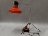 une lampe de bureau orange posée sur un pied métallique avec une base noire