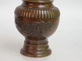 a bronze vase that is sitting on a white surface