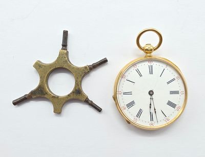 une montre de poche en or et une petite horloge posées sur une surface blanche