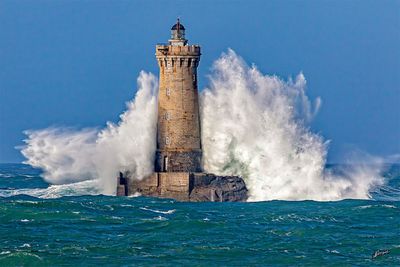un phare au milieu de l'océan, sur lequel vient s'écraser une grosse vague