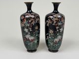 two black vases with flowers on them on a white surface