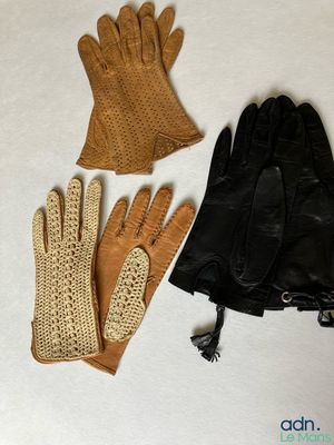 trois paires de gants en cuir et un sac à main posés sur une surface blanche