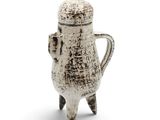 une cafetière blanche avec une anse, posée sur une surface blanche