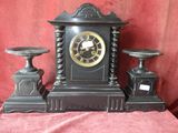 a black clock sitting on top of a table next to two candles