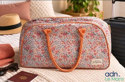 a floral bag sitting on a bed next to a hat and sunglasses