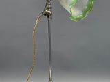 une lampe à l'ancienne avec un abat-jour en verre vert et une chaîne dorée