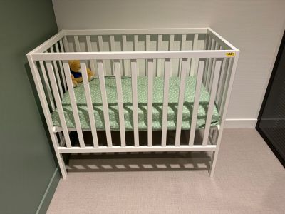 a white crib with a green sheet on it in the corner of a room