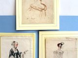trois dessins encadrés représentant des femmes en robe sur un mur bleu et blanc