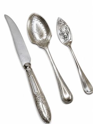 trois cuillères en argent et un couteau posés sur un plan de travail blanc