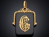 un pendentif en or et en onyxine orné de la lettre « g »