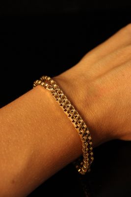 someone is holding a gold chain bracelet on their arm