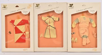 trois poupées dans leurs boîtes, vêtues de tenues différentes, présentées dans une vitrine