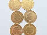 six pièces d'or sont disposées en ligne sur une surface blanche