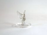 un petit oiseau argenté posé sur une assiette transparente, sur une surface blanche