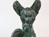 une statue verte représentant un chat assis sur une surface blanche