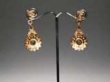 a pair of earrings with gold and diamonds on a stand