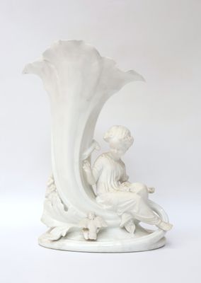 un vase blanc posé sur une table, sur laquelle est assise une femme