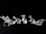 quatre oiseaux en verre posés sur une surface noire, sur fond noir