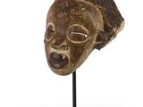 un masque africain posé sur un socle noir, sur fond blanc