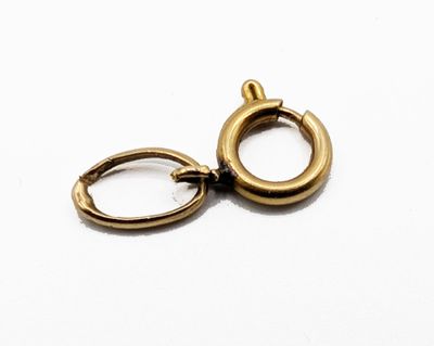 un gros plan sur une paire de boucles d'oreilles créoles en or posées sur une surface blanche