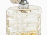 un flacon de parfum muni d'un bouchon métallique, posé sur une surface blanche