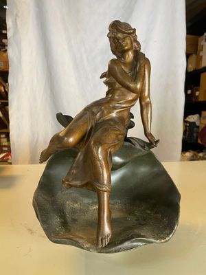 statue en bronze représentant une femme assise sur un rocher posé sur une table