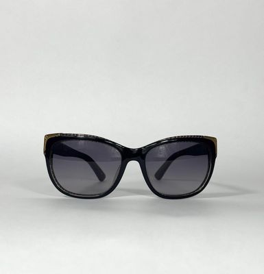 lunettes de soleil noires de style « œil de chat » avec des détails dorés sur fond blanc