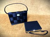 un sac à main et un portefeuille noirs posés sur un tissu beige, avec une bandoulière noire