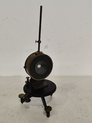 une photo représentant une lampe noire posée sur un pied, sur un sol blanc