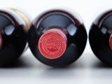three bottles of red wine sit side by side on a white surface