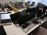 Plusieurs ordinateurs portables sont posés sur une table devant une rangée d'écrans