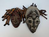 two african masks hanging on a wall next to a pile of sticks