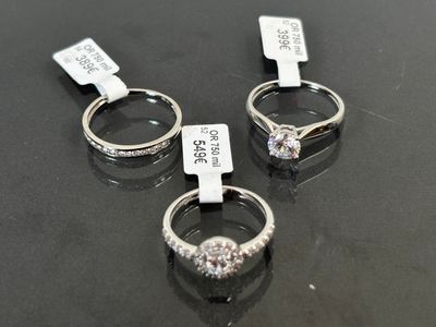 trois bagues en diamant, avec leurs étiquettes de prix, posées sur une table