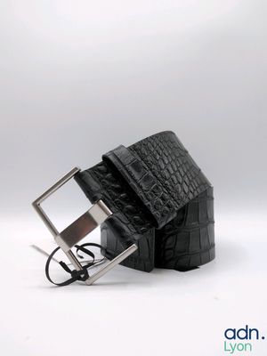 La ceinture est en cuir d'alligator noir et est dotée d'une boucle argentée.