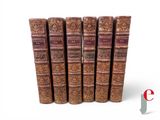 six vieux livres sont alignés sur une surface blanche