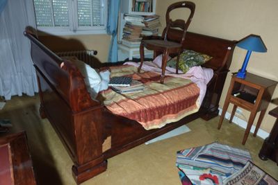 un lit qui se trouve dans une chambre où il y a beaucoup d'objets par terre