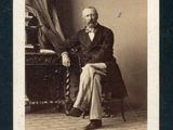 une vieille photo d'un homme en costume, assis sur une chaise