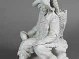 statue of a man sitting on a bench with a basket of grapes