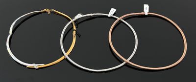 trois boucles d'oreilles en métal de couleurs différentes sur fond noir