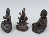 three bronze figurines of buddhas on a white surface