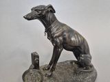 statue d'un chien assis sur un rocher, à côté d'un morceau de métal