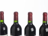 six bottles of red wine lined up in a row on a white surface