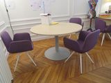 des chaises violettes disposées autour d'une table ronde dans une pièce aux murs blancs