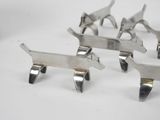 three silver metal dog figurines on a white surface