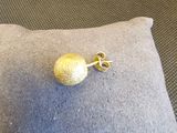 des boucles d'oreilles à clous en forme de boule dorée posées sur un coussin, sur un sol recouvert de moquette