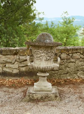 un vase en pierre posé sur un mur de pierre, près d'un mur de pierre