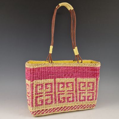 un sac en paille rose et jaune avec une anse marron sur fond gris
